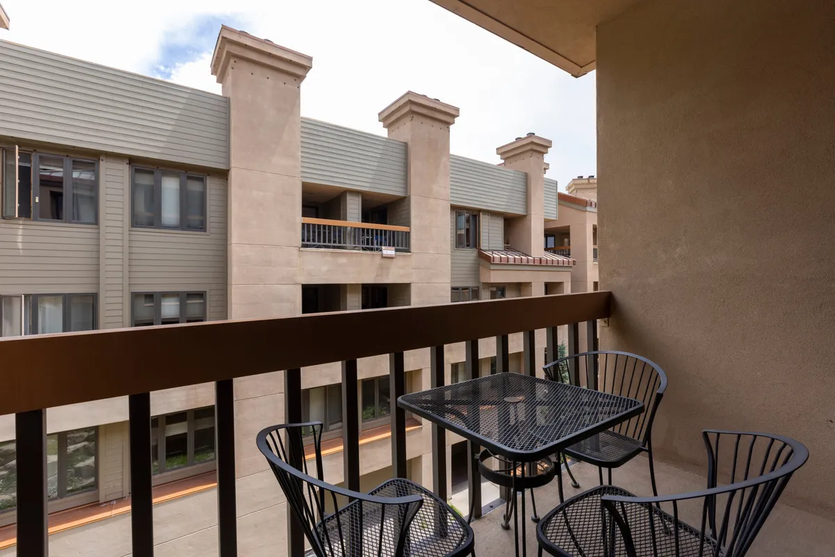 This image captures a welcoming balcony setup with a table and chairs, looking out over a neighboring building. The scene suggests a relaxed atmosphere, perfect for enjoying morning coffee, quiet reading, or sociable evenings with friends. The view connects guests to the vibrant surroundings of the mountain village.