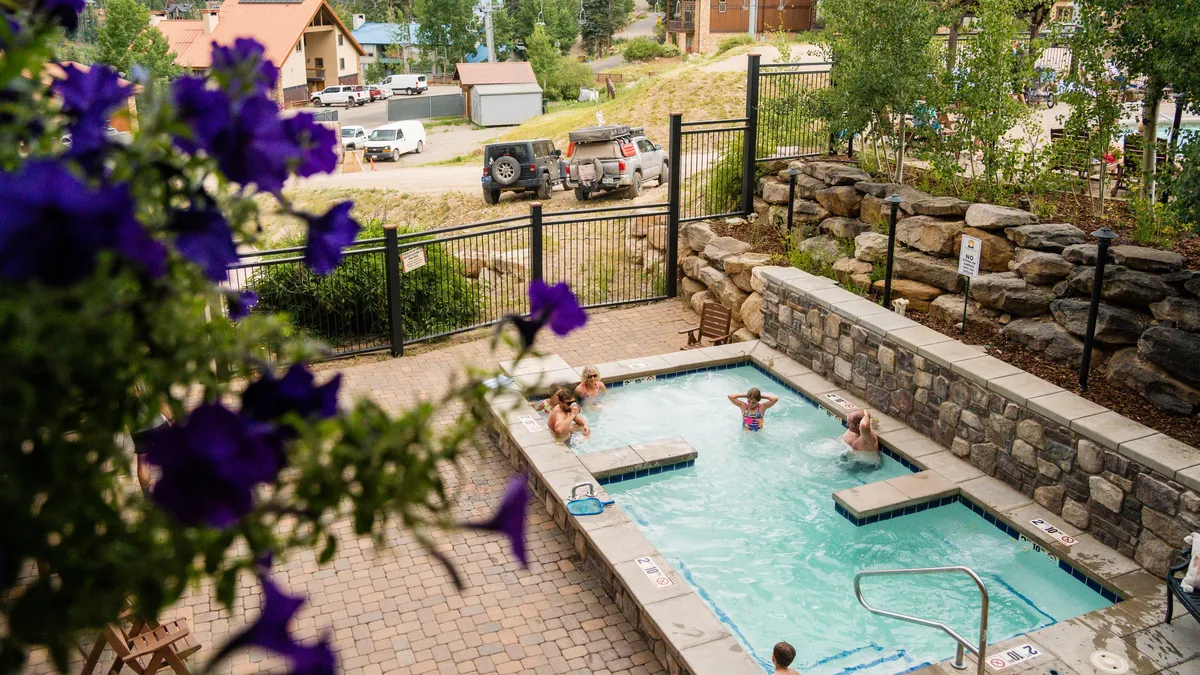 A scenic outdoor pool and hot tub area surrounded by flowering plants and the natural mountain landscape, creating a leisurely, inviting atmosphere.