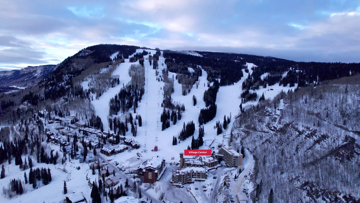 This exterior image captures the snow-covered slopes of Purgatory Resort, bustling ski lifts, and the inviting Village Center nestled among tall pine trees. The scene is lively with skiers and snowboarders, showcasing direct slope access from the village.