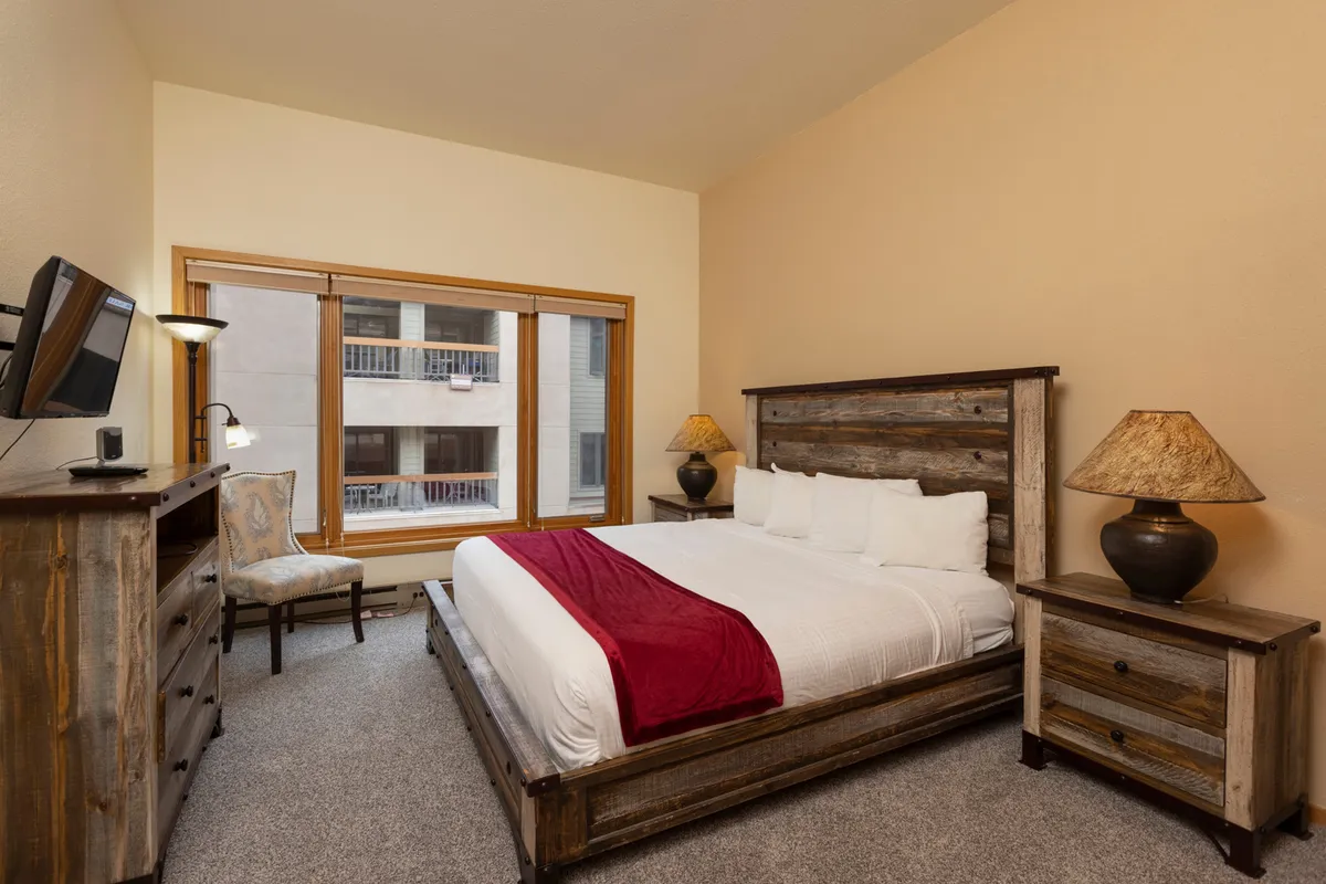 A serene bedroom setup with a comfortable bed, window offering a peaceful exterior view, nightstands, and a cozy chair. The space looks inviting, perfect for unwinding after a day outdoors, and provides flexibility for families or small groups.