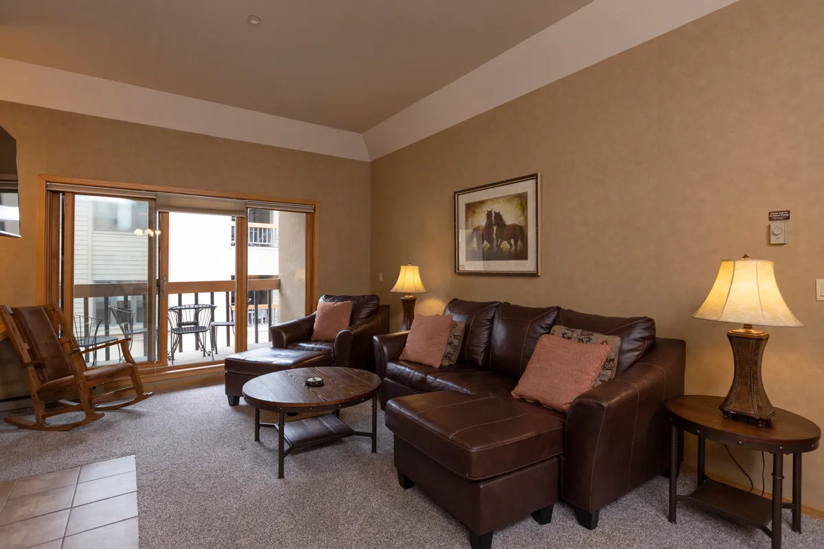 This image features a cozy living room with leather sofas, a rocking chair, a coffee table, a lamp, and wall artwork. The arrangement invites people to relax, read, or socialize in a welcoming, intimate setting.