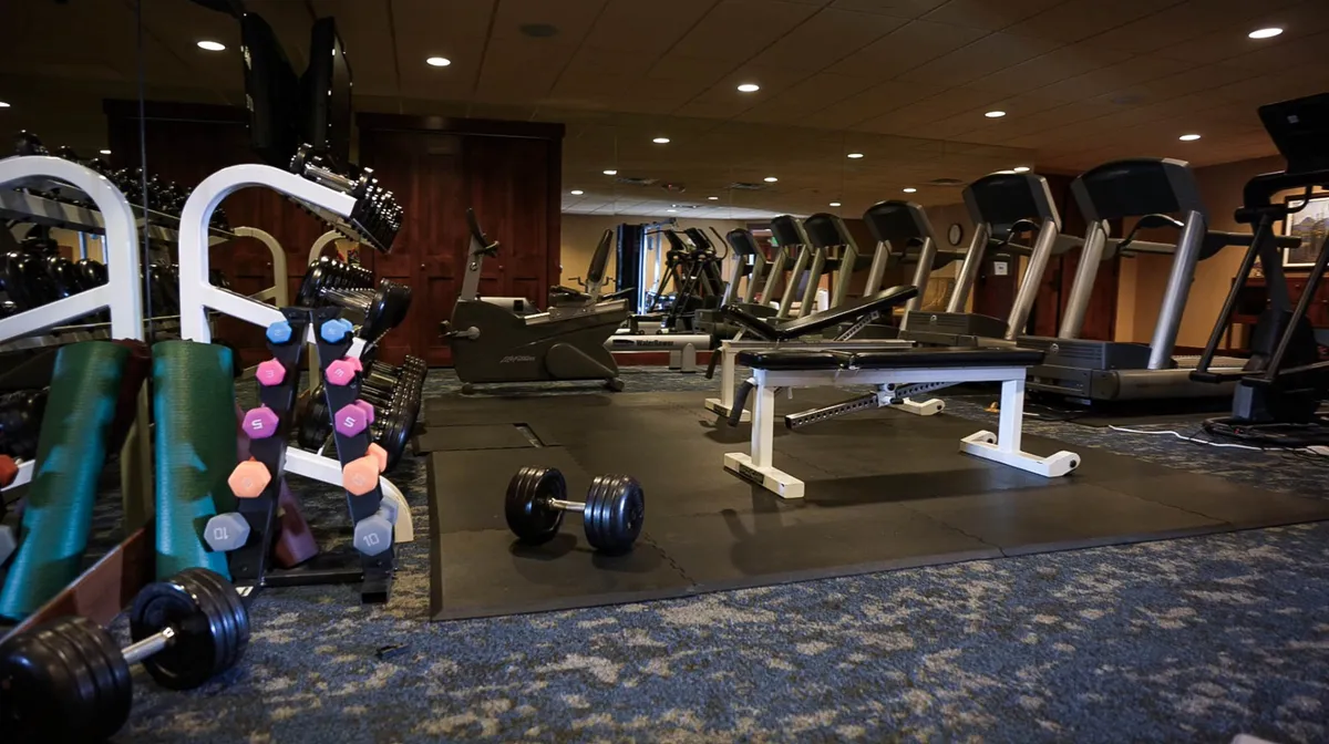 A modern, well-equipped fitness center featuring dumbbells, treadmills, and a weight bench, with clean lines and bright lighting creating an energetic environment.