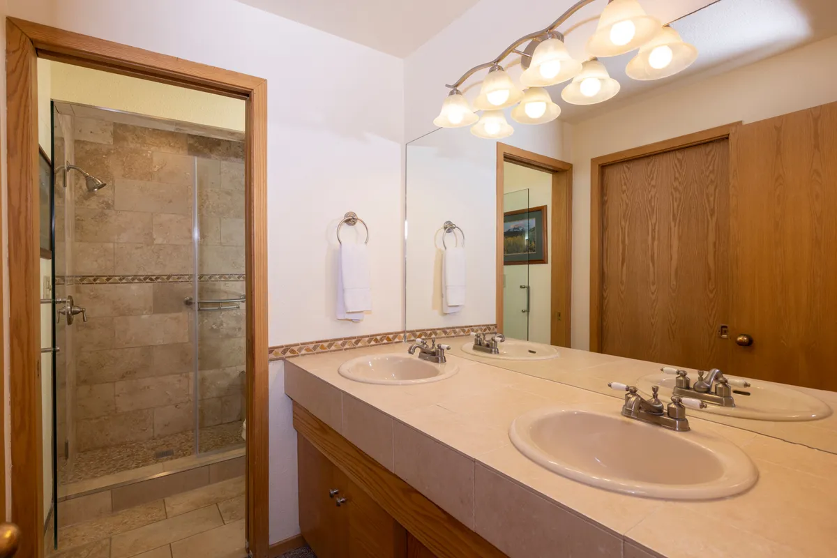 A well-organized bathroom featuring dual sinks, a spacious shower area, and a large mirrored surface. The clean and inviting design suggests easy morning and evening routines.